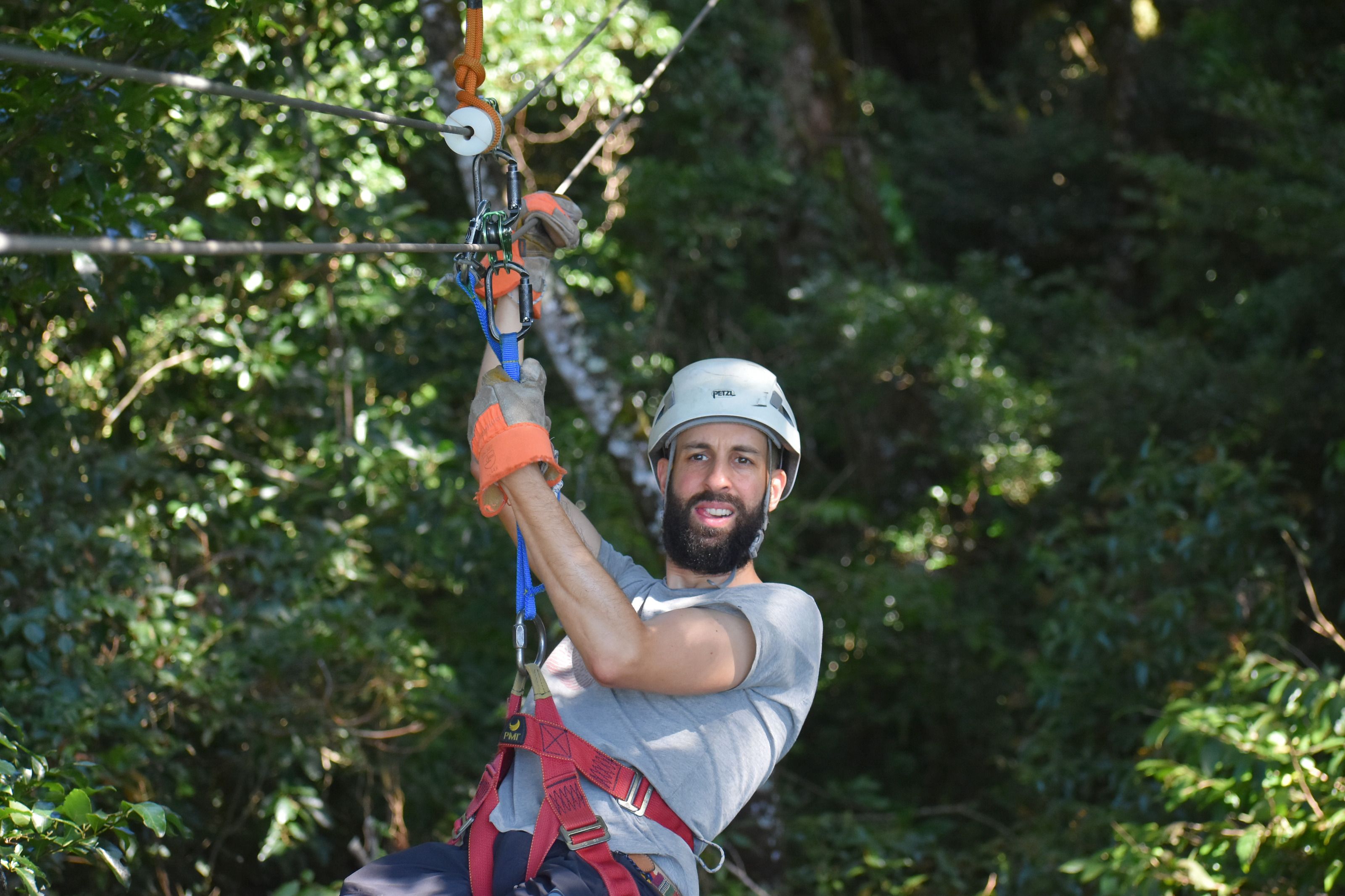 Nahaufnahme einer Person an der Zipline: Rolle, Gurt und die Hand im Handschuh am Seil